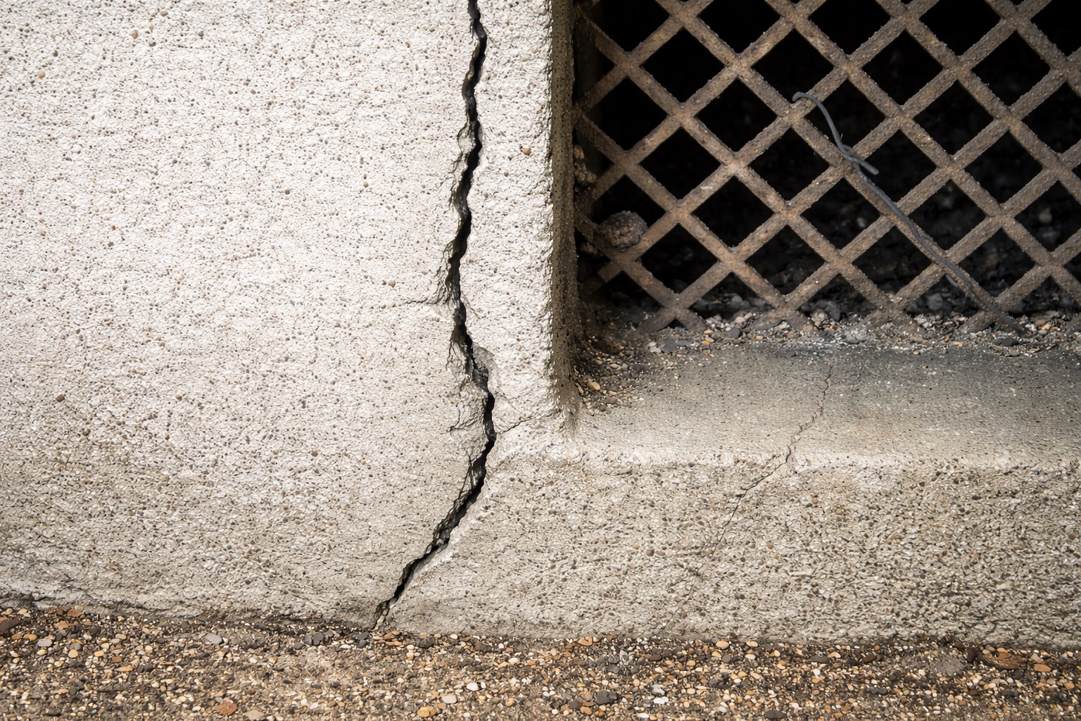 住宅基礎のコンクリート部分に発生した縦方向のひび割れと、近接する通気口まわりの劣化状況を写した基礎外周部の写真