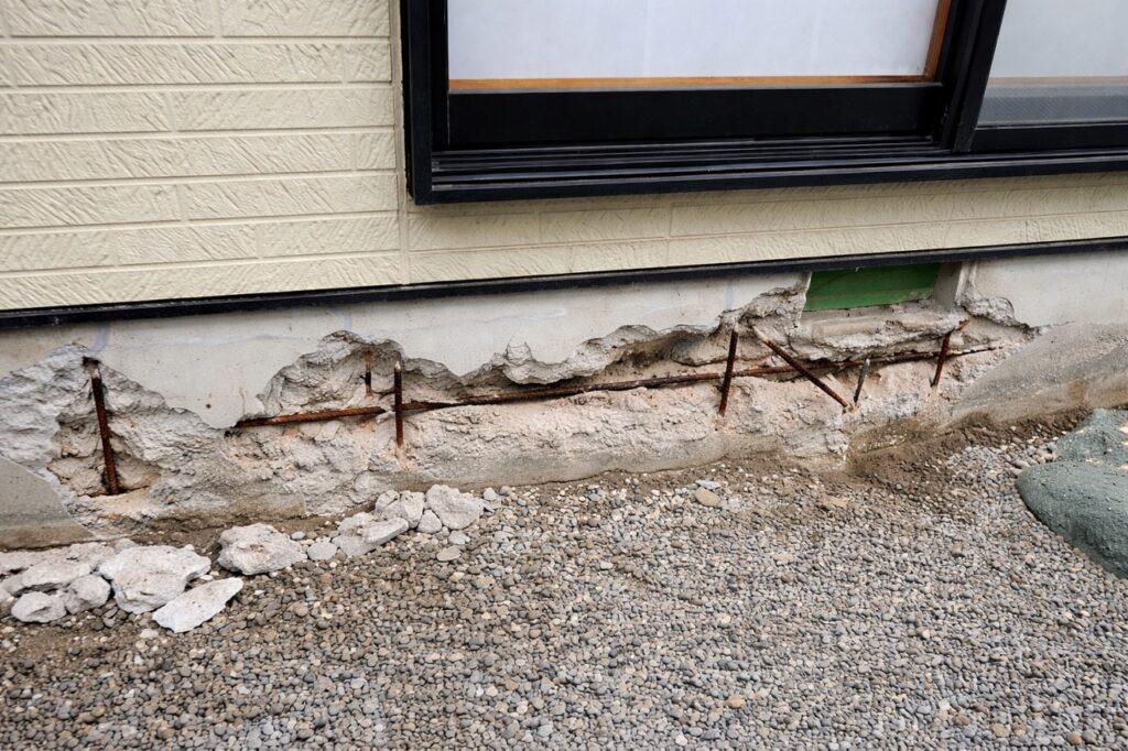 基礎コンクリートの爆裂現象により、コンクリートが剥がれて鉄筋が露出している戸建て住宅の基礎部分